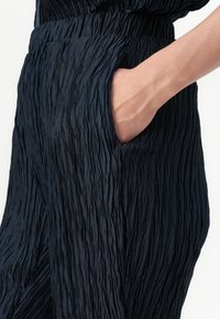 Pantaloni in tessuto textured blu navy con superficie increspata e tasca laterale, che presentano una vestibilità rilassata e una cintura elastica.