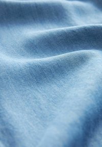 Hellblauer Stoff mit glatter Textur, leichtem Glanz und subtilen Farbvariationen, die sanfte Falten und Drapierungen zeigen.