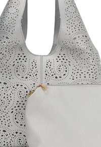 Lichtgrijze leren handtas met geperforeerde spiraalpatronen, voorzien van een ritszak en gouden hardware accenten. Zachte textuur en slappe ontwerp.