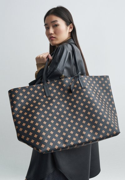 Grand sac fourre-tout en matière synthétique noire avec un motif géométrique beige, doté de deux poignées noires et d'un design structuré.