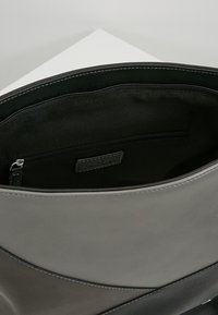 Interior de bolso de cuero gris con textura suave, bolsillo con cremallera y detalles sutiles de costura. Diseño limpio y minimalista.