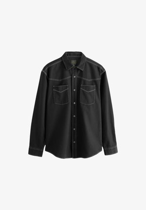 Chemise noire à boutons en tissu denim, avec des coutures blanches, deux poches poitrine et un col pointu avec des manches longues.