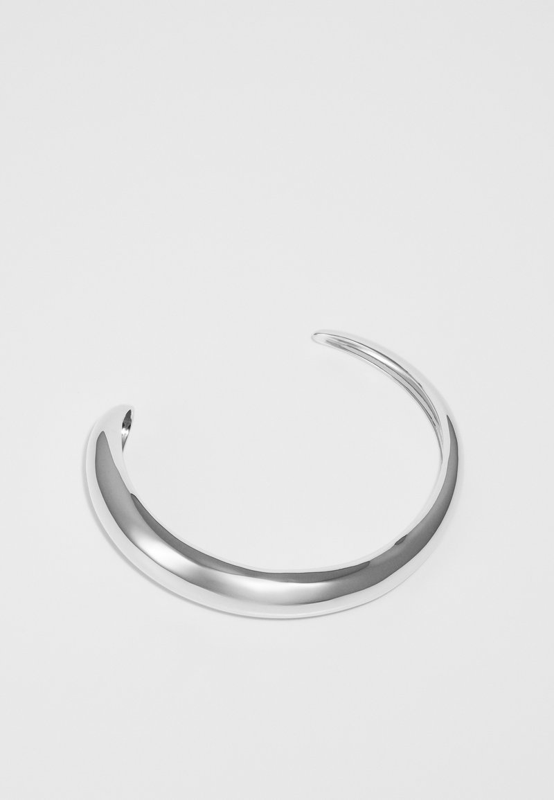 Stříbrný kovový náramek s leštěným povrchem, s hladkým, zaobleným designem a otevřenými konci pro nastavitelnou velikost.