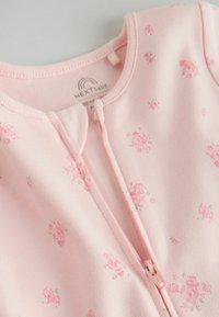 Tutina morbida rosa per neonati con piccoli motivi floreali e chiusura frontale con cerniera, prodotta da NEXT baby.