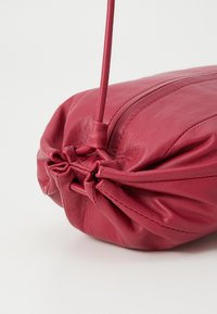 Rød lædertaske med en sammenskrumpet design, glat tekstur og tynd rem. Kendt for sin bløde form og lette glans.