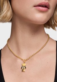 Collier en perles dorées avec un pendentif en forme d'ours, agrémenté d'accents noirs et dorés. Le pendentif présente un motif texturé.