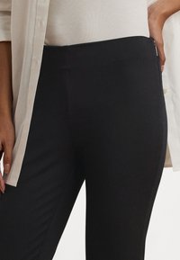 Melnas legingas no elastīga, gluda auduma ar augstu vidukli. Aprīkotas ar sānu rāvējslēdzēju un pieguļošu dizainu.