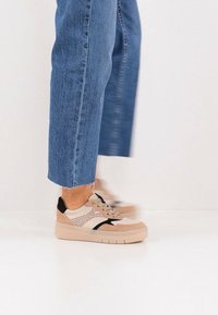 Μπεζ και μαύρα αθλητικά παπούτσια με λεπτομέρειες από δίχτυ και σουέντ, παχιά σόλα πλατφόρμας, σχέδιο με κορδόνια, συνδυασμένα με κοντά μπλε τζιν παντελόνια.