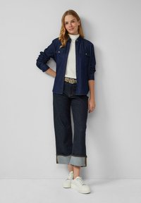 Donkerdenim knoopshirt met borstzakken, gecombineerd met wijde donkere jeans met opgerolde zoom en witte sneakers.