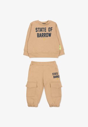 Beżowa polarowa bluza i dopasowane spodnie z napisem "STATE OF BARROW" w ciemnoniebieskim kolorze. Spodnie mają kieszenie cargo i ściągacze przy nogawkach.