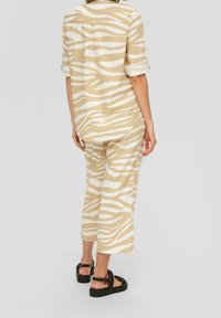 Camicia a righe zebra marrone chiaro e bianco con maniche arrotolate, abbinata a pantaloni larghi coordinati. Sandali con piattaforma neri completano l'outfit.