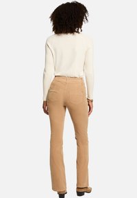 Pantalones de pana marrón claro con corte acampanado, bolsillos traseros y cintura alta, combinados con un suéter ajustado de color crema. Tejido texturizado, diseño limpio.