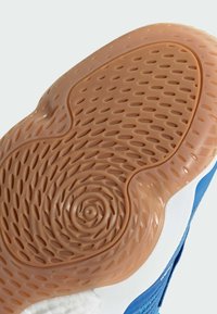 Podešev boty s texturovanou gumou v světle oranžové barvě, s kruhovými a oválnými vzory, a modrou horní částí viditelnou podél okraje.