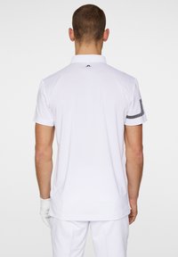 Weißes kurzärmliges Poloshirt mit klassischem Kragen, das ein strukturiertes Design und ein schwarzes Streifendetail am Ärmel aufweist.