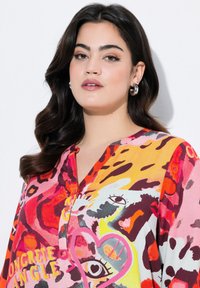 Chemise à motifs présentant des couleurs vives telles que le rose, le jaune et le rouge, avec des designs abstraits et un col, fabriquée à partir d'un tissu léger.