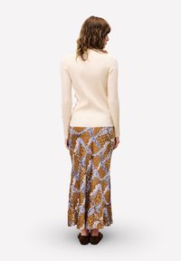 Crèmekleurige geribde trui, lange mouwen; bruine maxi rok met een patroon en blauwe accenten; zacht materiaal, getailleerde pasvorm, zijsplitsingen bij de zoom.