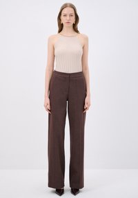 Beige ribbel mouwloos topje gecombineerd met high-waisted, wijdvallende bruine broek, met een subtiele textuur en klassieke snit.