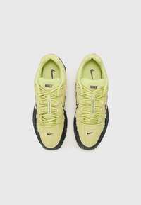 Tênis Nike com parte superior amarelo claro, malha texturizada e detalhes em camurça, sola preta e acentos pretos nos cadarços e no logotipo.