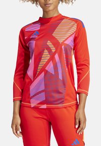 Rode sporttop met lange mouwen, voorzien van geometrische patronen in roze, oranje en blauw. Gemaakt van gestructureerde, ademende stof.