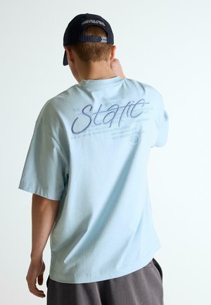 Osoba otočená chrbtom, ktorá nosí svetlomodré tričko s nápisom „Staff“ a čiernu čiapku s bielym nápisom.