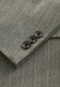 Manche de costume gris à fines rayures avec trois boutons ronds foncés cousus près du poignet sur un tissu tissé texturé.