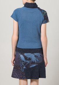 Robe bleue avec un col montant, des manches courtes et une partie inférieure à motifs présentant des nuances de bleu et un tissu foncé. Texture douce.