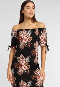 Vestido negro sin hombros con estampado floral en tonos melocotón y crema. Presenta mangas cortas con detalles de lazos y un diseño ajustado.
