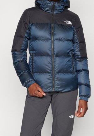 Marine blauwe pufferjack met zwarte accenten, voorzien van een hoge kraag, ritszakken en elastische manchetten, ontworpen voor warmte en comfort.