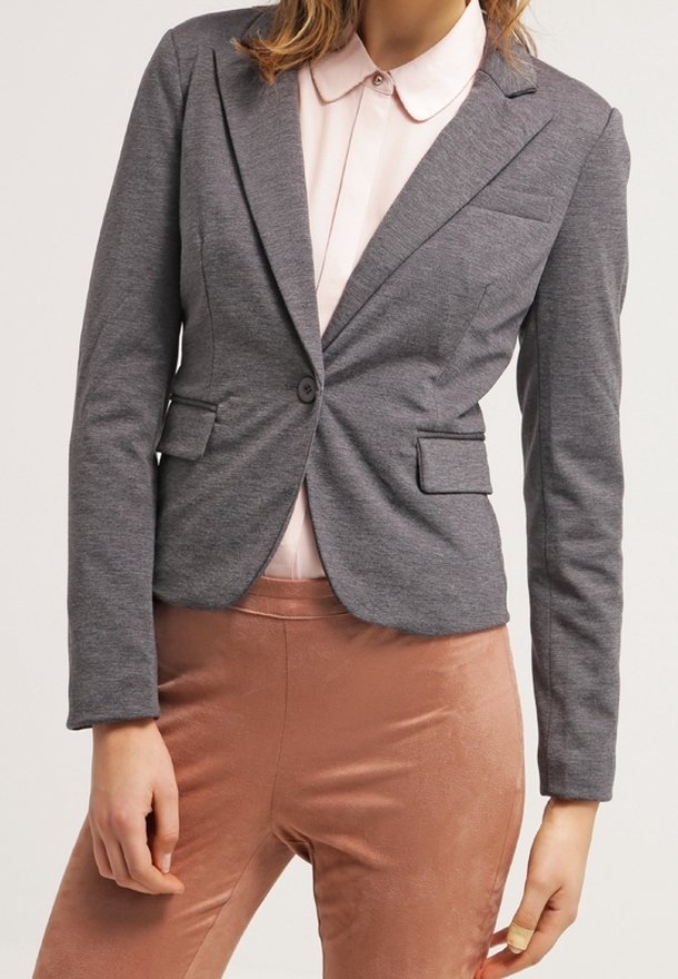 Blazer gris cintré avec deux poches avant et une fermeture à un bouton, porté sur une chemise à col rose clair et un pantalon couleur pêche.