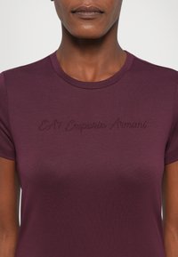 Burgundské tričko s krátkým rukávem vyrobené z měkké tkaniny, s vyšitým logem "EA7 Emporio Armani" v odpovídající nitě na hrudi.
