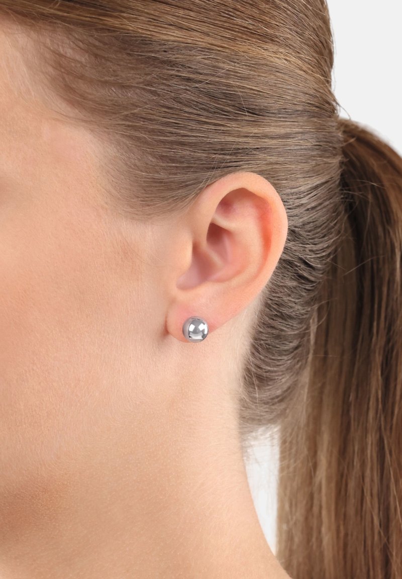 Silverfärgad metallstiftörhänge visat på ett öra. Rund form med en polerad, reflekterande yta som framhäver en slät textur.