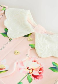 Svetloružové šaty s bielym čipkovaným golierom, kvetinový vzor s pivonkami, zlaté srdiečkové detaily a štruktúrovaná tkanina.