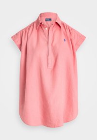 Camicia di lino rosa con colletto corto, maniche arrotolate e un piccolo logo blu sul petto. Caratterizzata da una vestibilità ampia e rilassata e un orlo morbido.