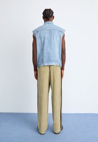 Denimvest med ærmeløs design, lys tvætning, frynset kant, parret med olivengrønne brede bukser med sorte sidestriber.