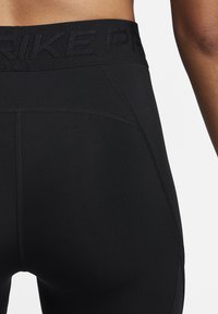 Zbliżenie na dolną część pleców i biodra osoby noszącej czarne legginsy sportowe z widocznym szwem i logo "NIKE PRO" na pasku.