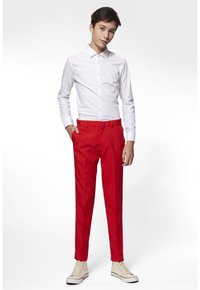 Camicia bianca con bottoni, pantaloni rossi, taglio slim; tessuto morbido; modello posizionato con una mano in tasca, indossando sneakers chiare.