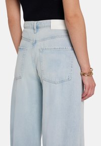 Jeans azzurri a vita alta con un fit rilassato, dotati di due tasche posteriori e di un'etichetta bianca del marchio in vita. Tessuto denim liscio.