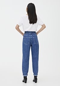 Jeans de mezclilla azul de cintura alta con una pretina elástica fruncida, piernas estrechas y dobladillos enrollados, combinados con una camisa blanca de manga corta.