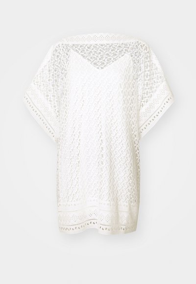 Bela, ohlapna majica iz čipkastih tkanin z geometrijskimi vzorci, kratkimi rokavi in dekorativnim robom z izrezljanimi akcenti.