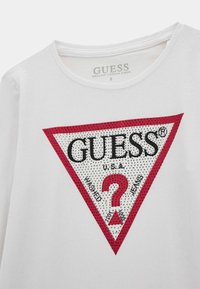 Weißes T-Shirt aus Bio-Baumwolle mit einem dreieckigen roten und schwarzen Logo, verziert mit Strasssteinen, mit der Aufschrift "GUESS USA" und "Washed Jeans."