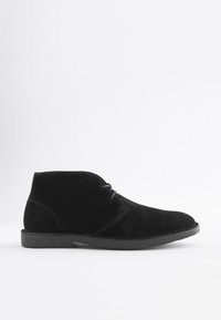 Schwarzer Veloursleder-Stiefelette mit Schnürung vorne und niedriger Gummisohle, seitlich auf weißem Hintergrund gezeigt.
