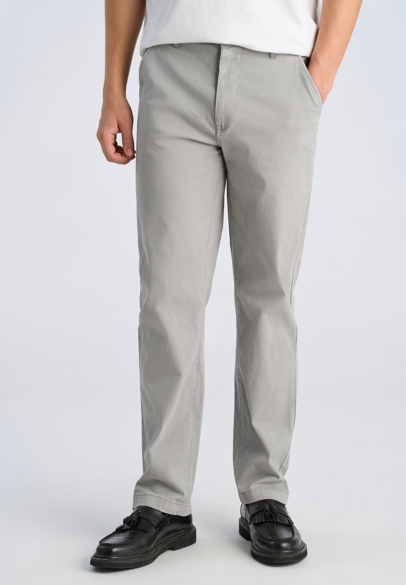 Graue Baumwoll-Chinos mit Gürtelschlaufen und Seitentaschen, gerade geschnitten, kombiniert mit schwarzen Loafers mit Fransenakzenten.