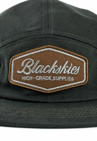 Fekete sapka textúrált anyagból, jellegzetes barna hímzett folttal, rajta a "Blackskies" és a "HIGH-GRADE SUPPLIES" felirattal fehér színben.