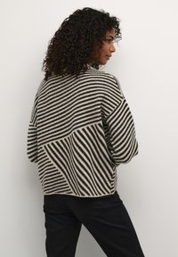 Pull en maille rayé beige et noir, présentant une coupe décontractée, des manches surdimensionnées et un motif texturé. La vue de dos montre les détails du design.
