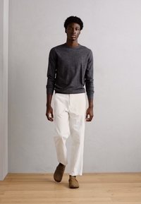 Charcoalgrå langærmet trøje, hvide plisserede bukser og brune slip-on sko. Glat tekstur, afslappet pasform, casual design.