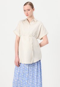 Blusa a righe beige e bianca a maniche corte con vita annodata, abbinata a una gonna blu con fiori e bottoni bianchi.
