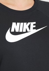 Svart bomulls-t-shirt med en framträdande vit "NIKE"-logotyp och swoosh-design på bröstet, med en klassisk rund halsringning och korta ärmar.