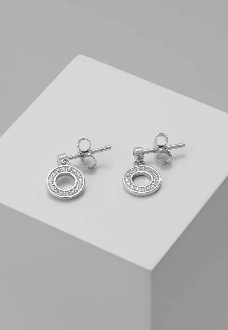 Paire de boucles d'oreilles clous en argent avec petits pendentifs circulaires incrustés de minuscules pierres, présentée sur un fond cube blanc.