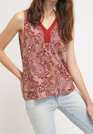 Top sin mangas con un patrón de paisley en rojo y beige, con un escote en V texturizado. Material ligero. Combinado con jeans de color azul claro.