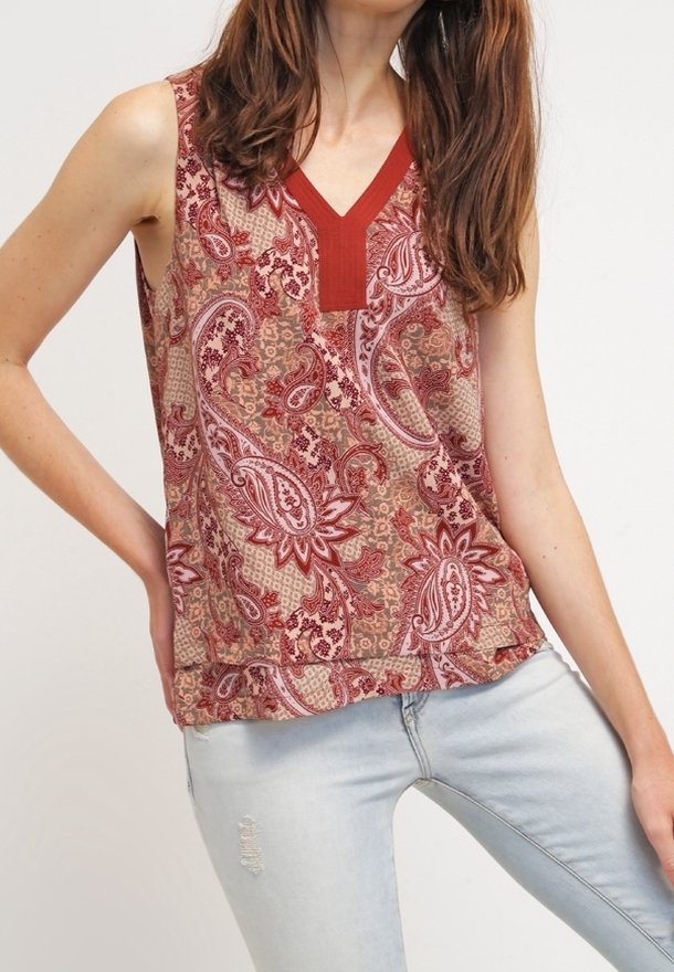 Top senza maniche con un motivo paisley rosso e beige e una scollatura a V testurizzata. Materiale leggero. Abbinato a jeans azzurri chiari.